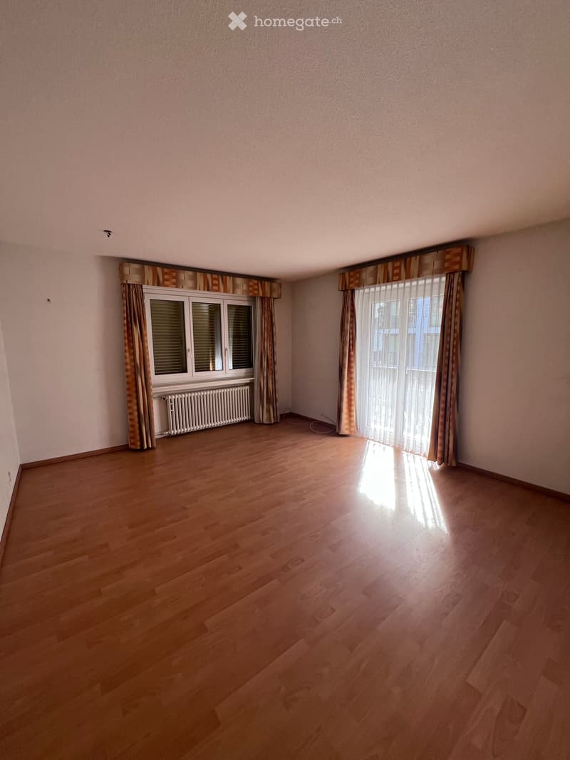 Empty room with wooden flooring, light pink walls, and two windows with curtains. A radiator is visible under one window.