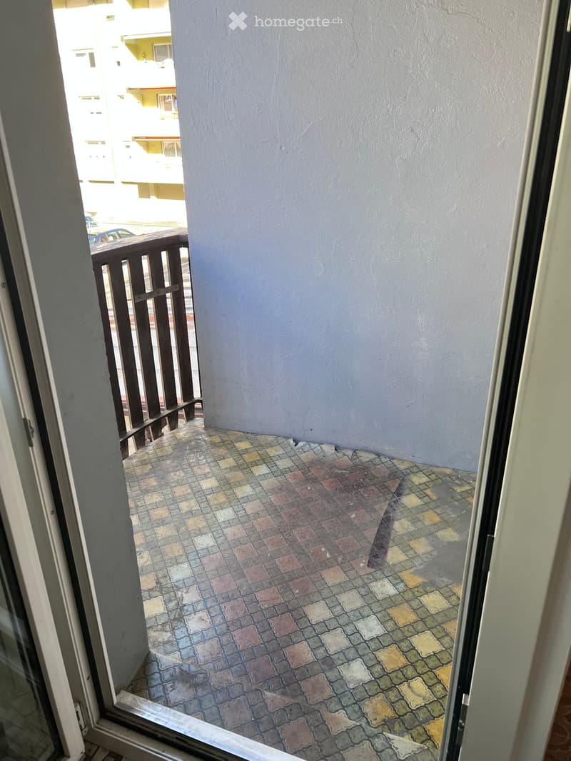 Balcony with colorful tiled floor, wooden railing, and view of neighboring buildings.