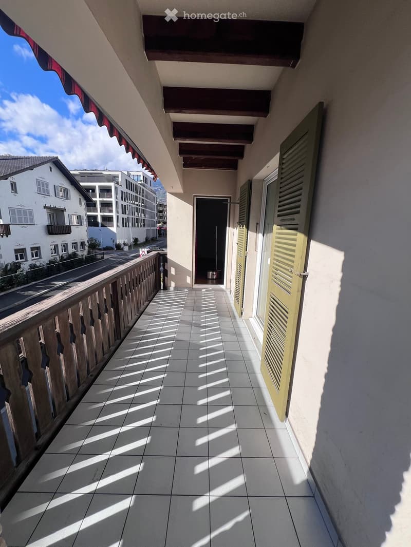 Balcony with tiled floor, wooden railing, and open shutters leading to an interior space.