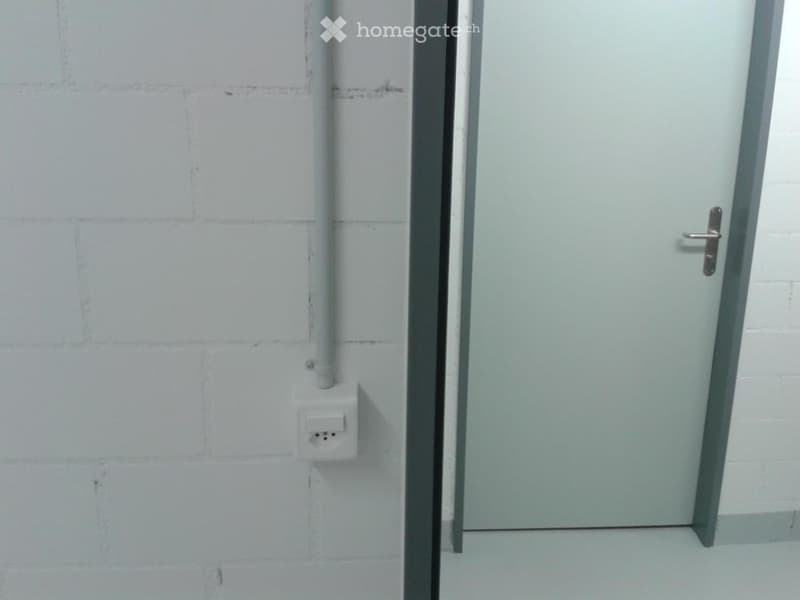 Empty room with white brick walls, a closed door, and a power outlet on the wall.