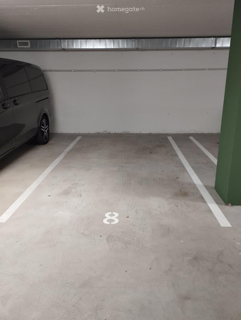 Underground parking space with marked parking spots, a single car parked on the left side, and a green support pillar on the right.
