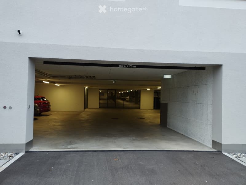 Entrance to an underground parking garage with a red car partially visible inside, concrete floors, and modern lighting.