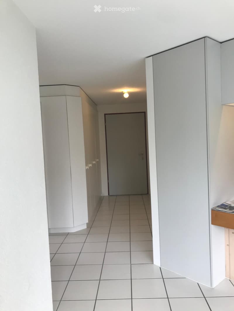 Empty hallway with white tiled floor, white walls, and a closed door at the end.