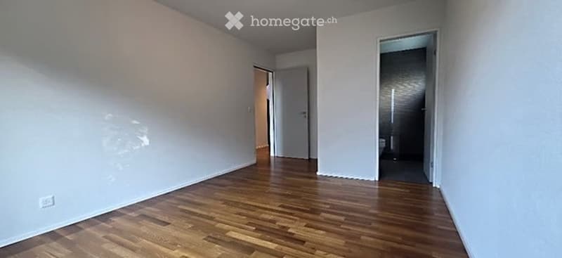 Empty room with wooden flooring and white walls, featuring two open doorways leading to adjacent spaces.