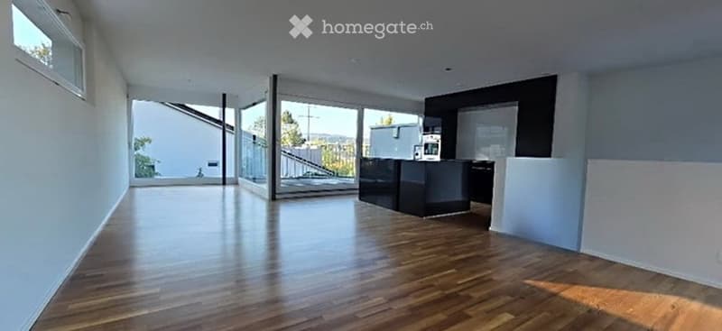 Open-plan space with wooden flooring, large windows, and a small black counter. No furniture or equipment visible.