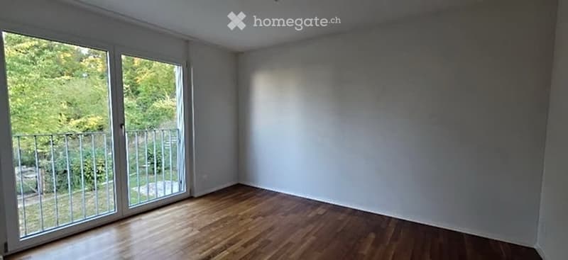 Empty room with wooden flooring, large windows, and a balcony access. No furniture or equipment present.