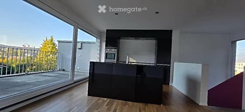Modern kitchen with a black island, built-in oven, and large windows offering a view of the balcony and outdoor area.