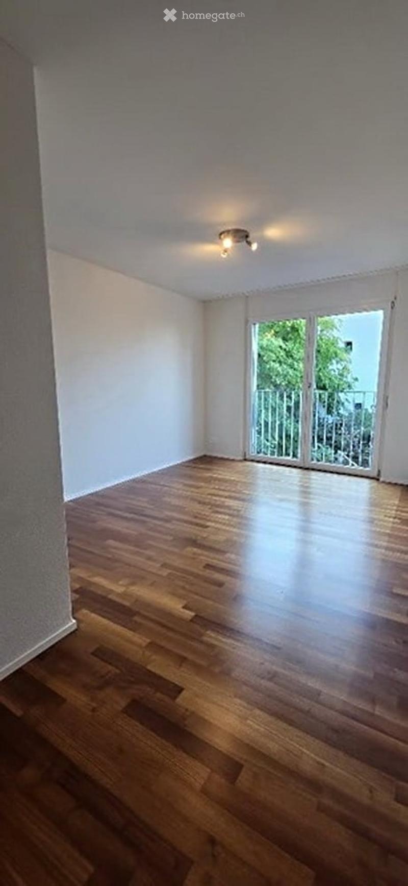 Empty room with wooden flooring, white walls, and a sliding glass door leading to a balcony.