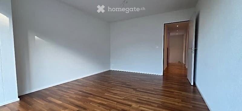 Empty room with wooden flooring and white walls, featuring a doorway leading to a hallway.