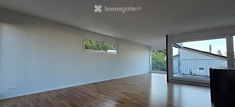 Empty room with wooden flooring, white walls, large window, and sliding glass door leading to a balcony.