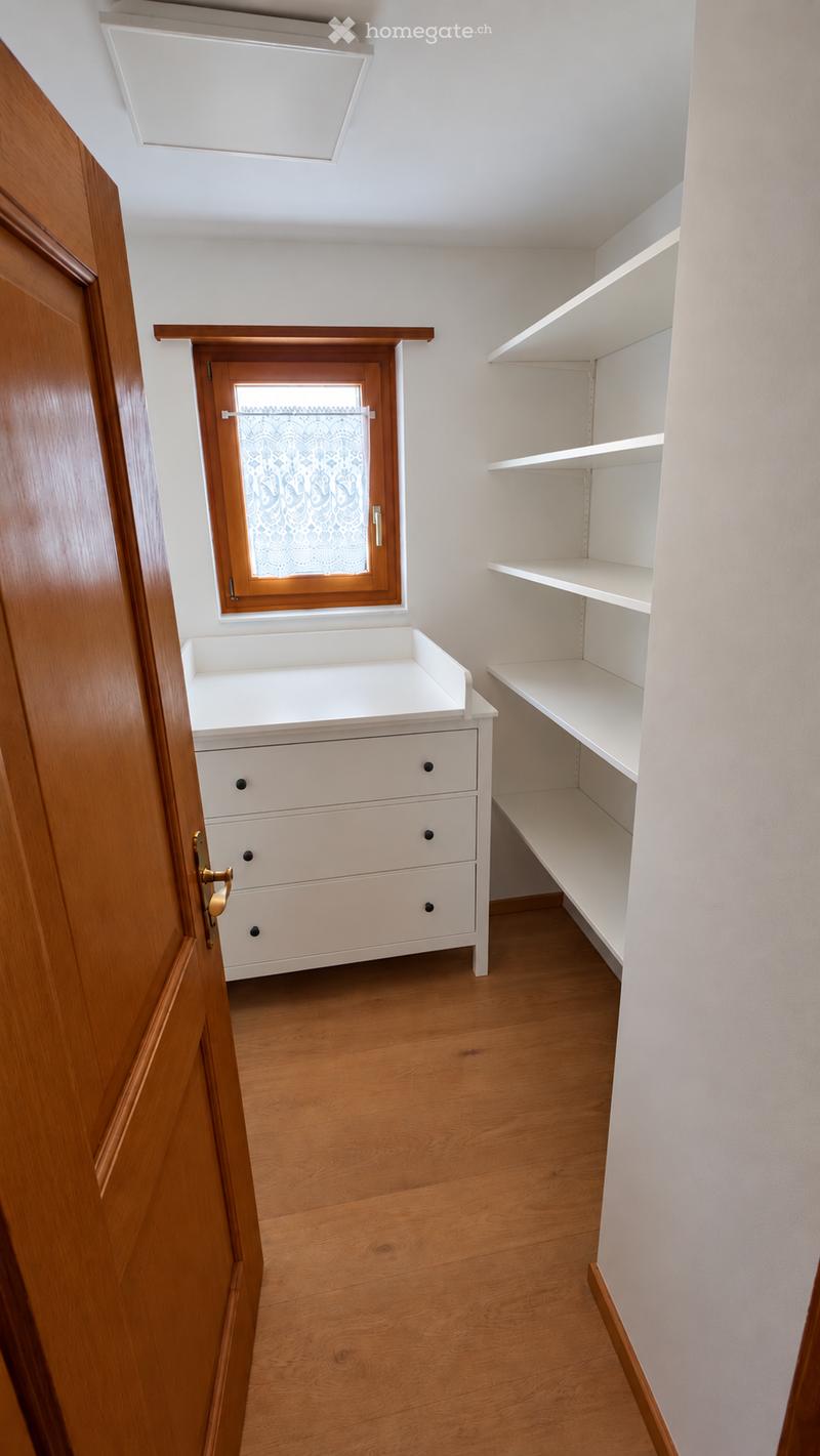 Empty closet with wooden floor, white walls, built-in shelves, and a small white dresser with drawers.