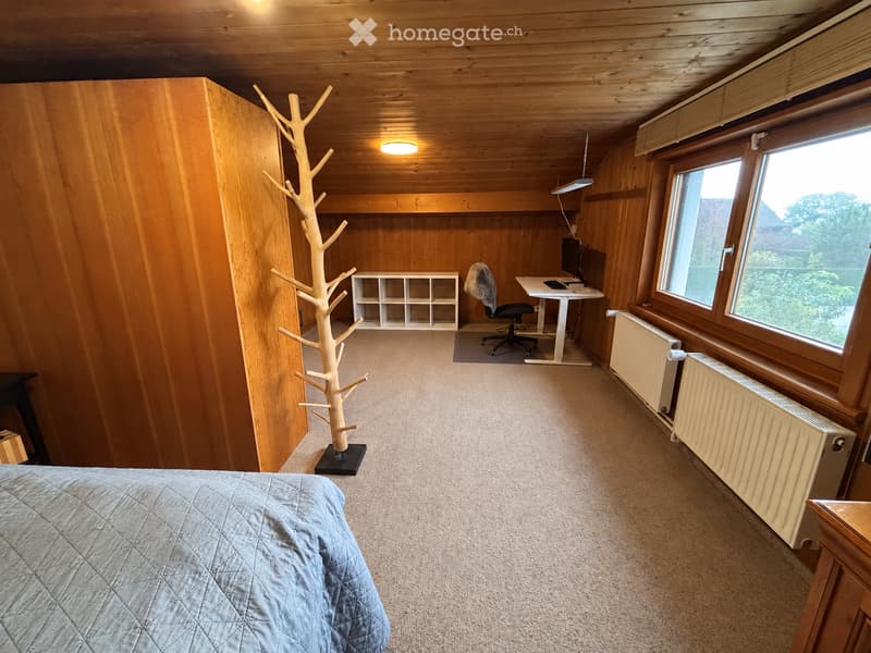 Cozy room with wooden walls and ceiling, featuring a bed, desk with a computer, a chair, a coat rack, and a shelf.