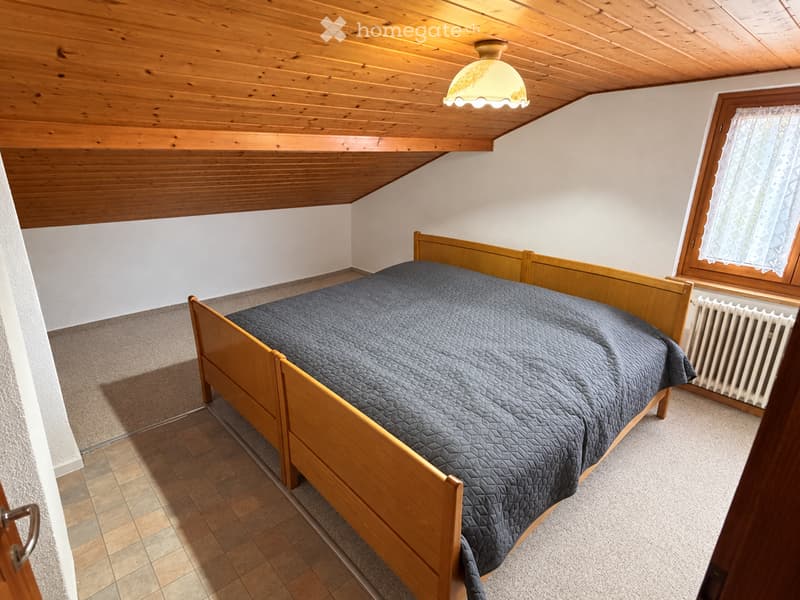 Cozy bedroom with wooden bed, dark blue quilt, wooden headboard, radiator, and wooden slanted ceiling.