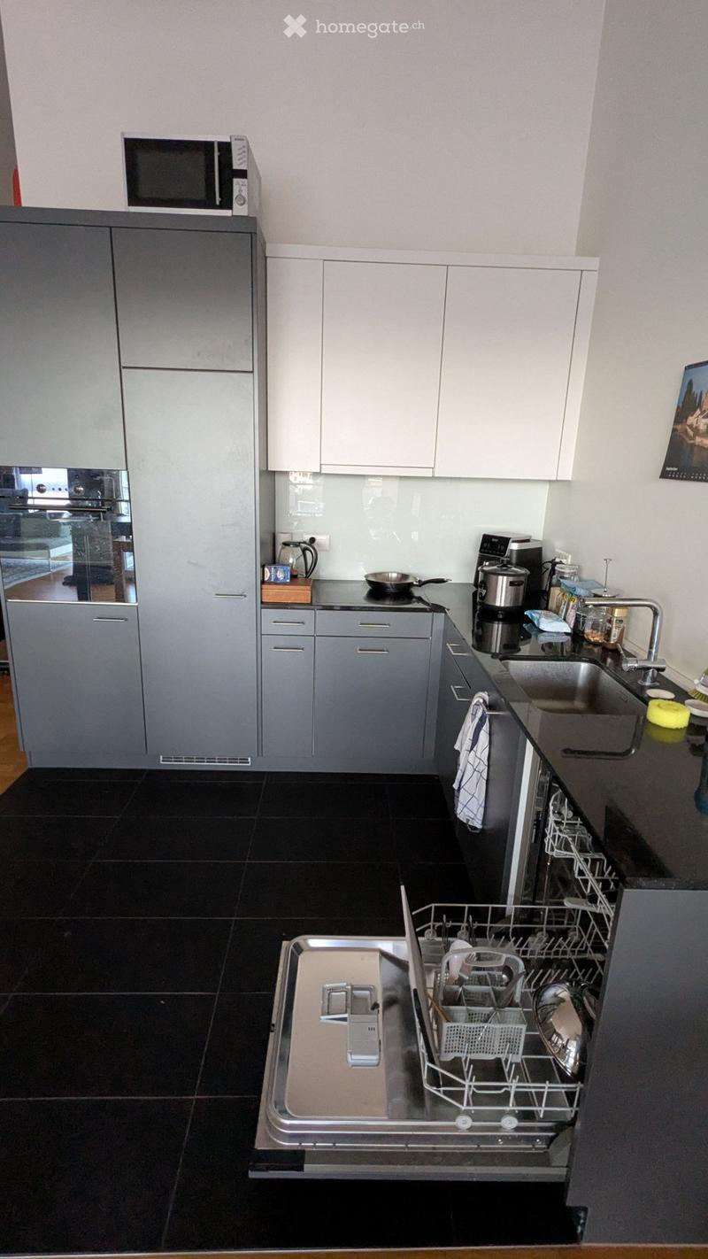 Modern kitchen with grey cabinets, black tiled floor, stainless steel sink, dishwasher, microwave, and coffee maker on the counter.