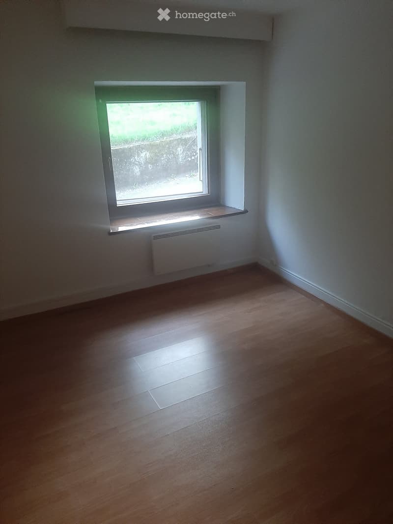 Empty room with wooden flooring, white walls, a window with a radiator below, and a small shelf on the windowsill.