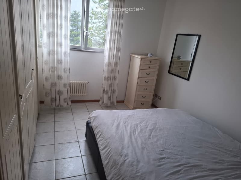 Bedroom with a single bed, dresser, mirror, and radiator. Light-colored walls and tiled floor.