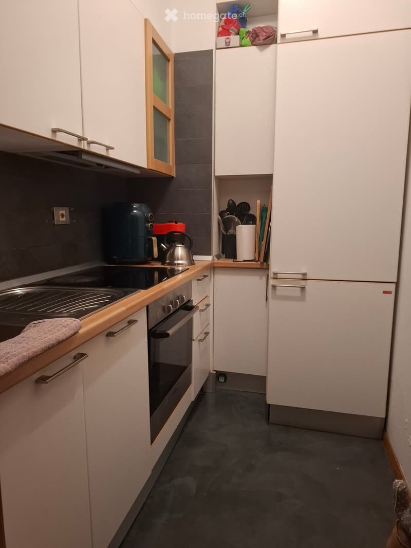 Modern kitchen with white cabinets, stainless steel appliances, and a dark grey tiled backsplash. Includes an oven, stove, coffee maker, kettle, and various kitchen utensils.