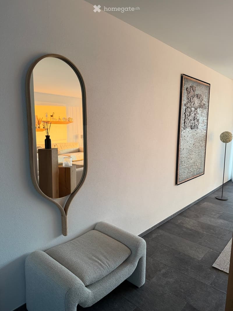 Modern hallway with a grey sofa, large round mirror, abstract artwork, and a floor lamp.
