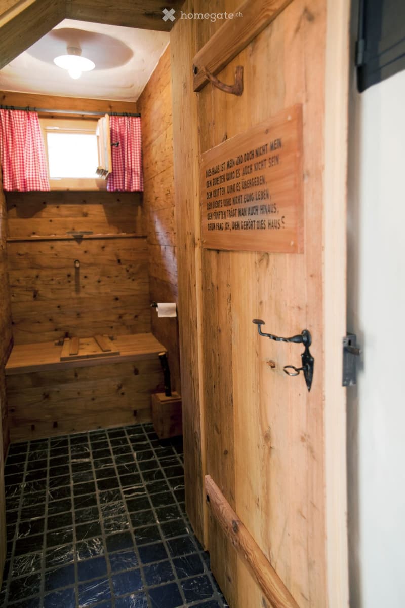 Wooden bathroom with a bench, toilet paper, and a window with red checkered curtains.