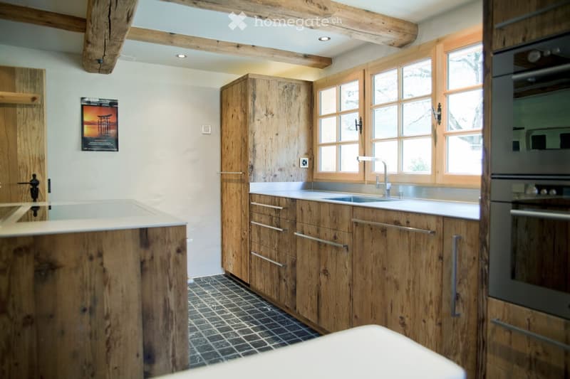 Modern kitchen with wooden cabinets, stainless steel sink, and oven. Features a central island with a marble countertop and a black tiled floor.