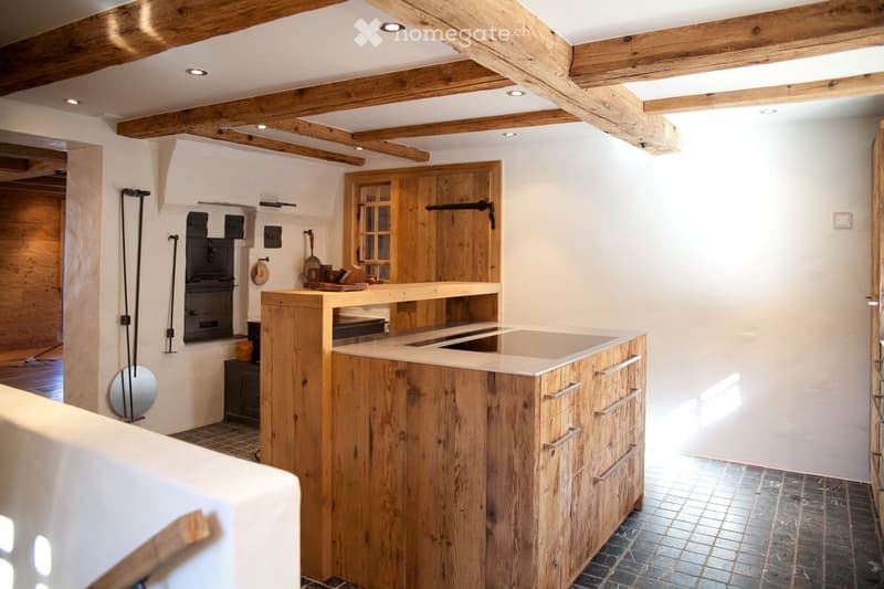 A rustic kitchen with wooden beams, a wooden counter, sink, and cabinet. Includes a mirror, frying pan, and oven.