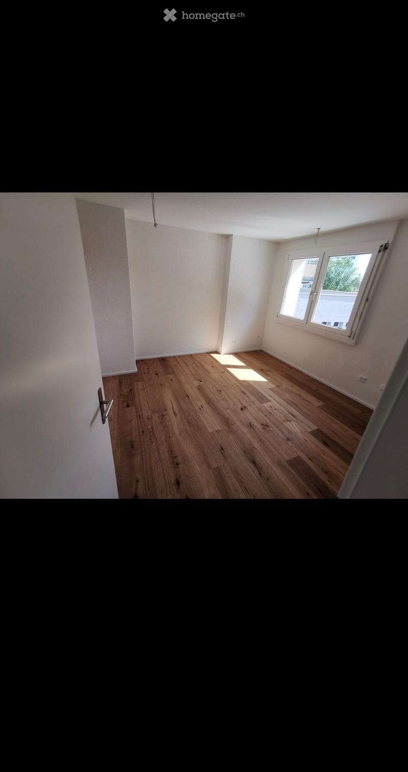 Empty room with wooden flooring, white walls, and two windows allowing natural light to enter.