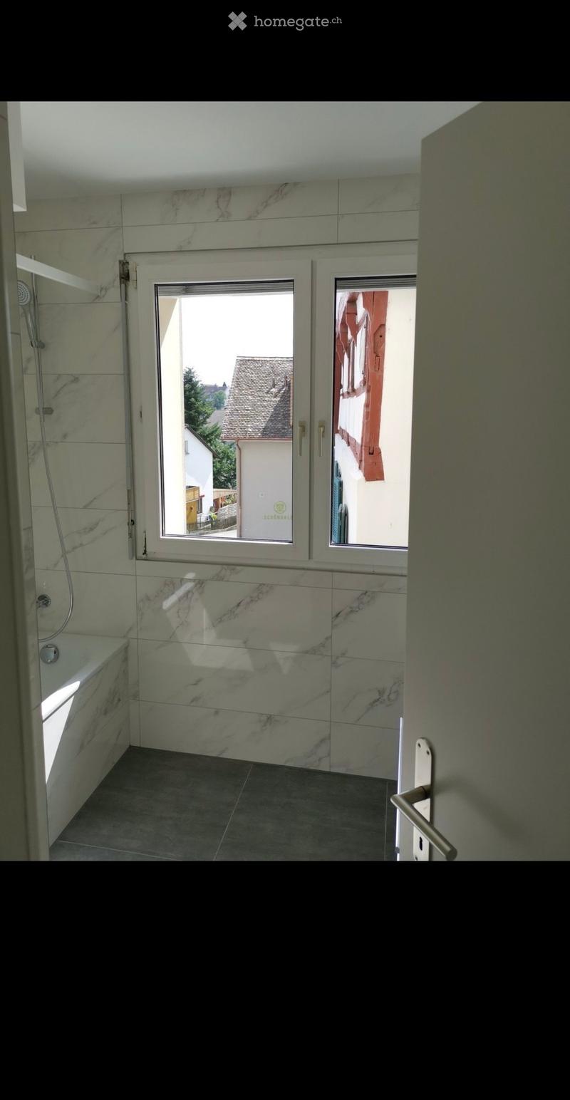 Modern bathroom with marble tiles, bathtub, shower, and large windows offering a view of the street.
