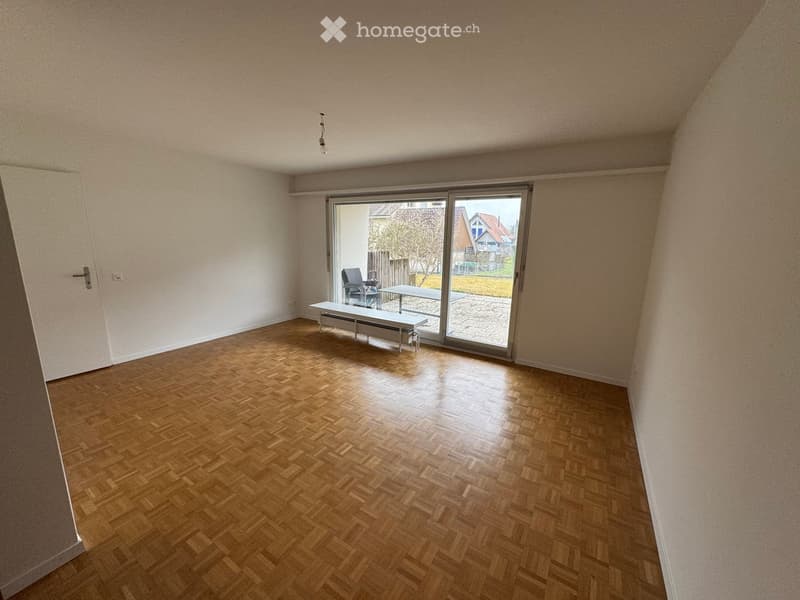 Empty room with wooden herringbone flooring, white walls, and a large sliding glass door leading to a patio area.