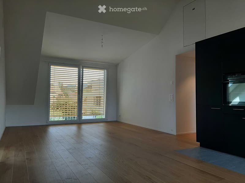 Empty room with wooden flooring, large window with blinds, and built-in cabinetry.