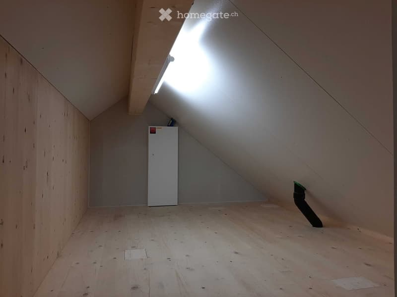Empty attic space with wooden walls and floor, exposed beams, and a small window letting in natural light.