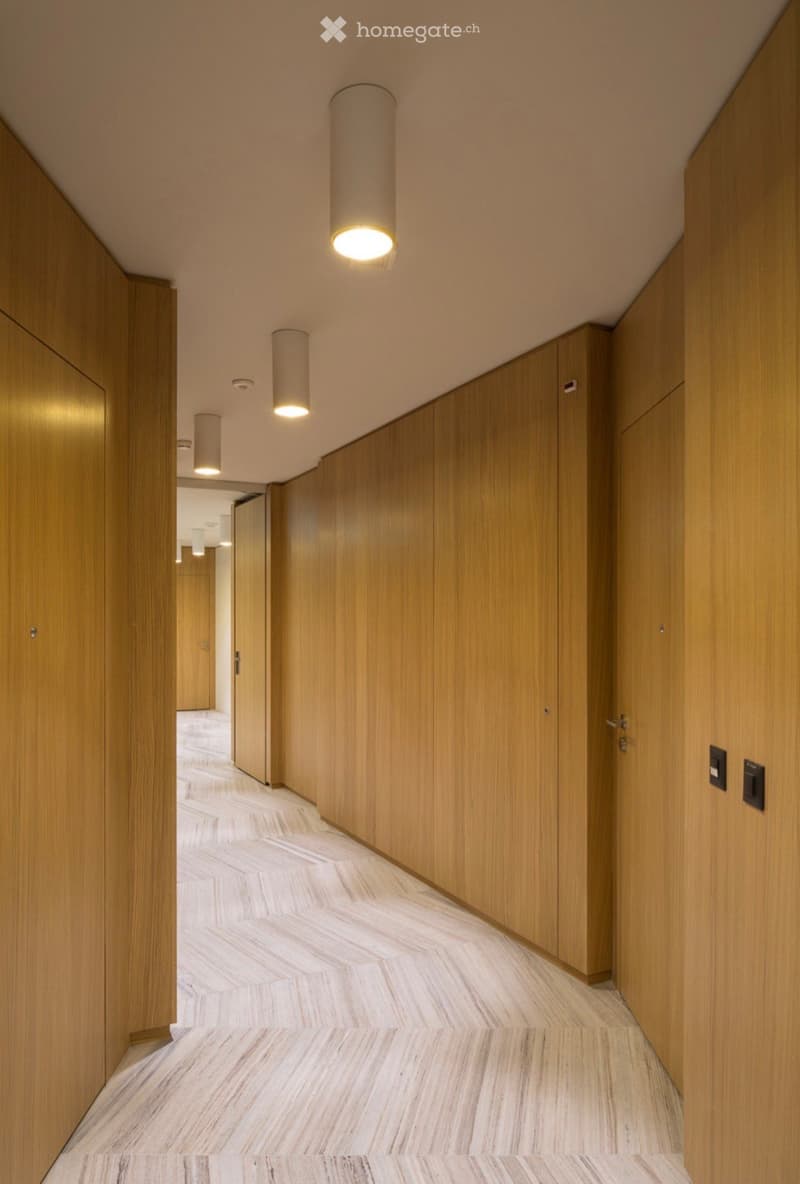 Modern hallway with wooden panel walls, marble flooring, and cylindrical pendant lights.