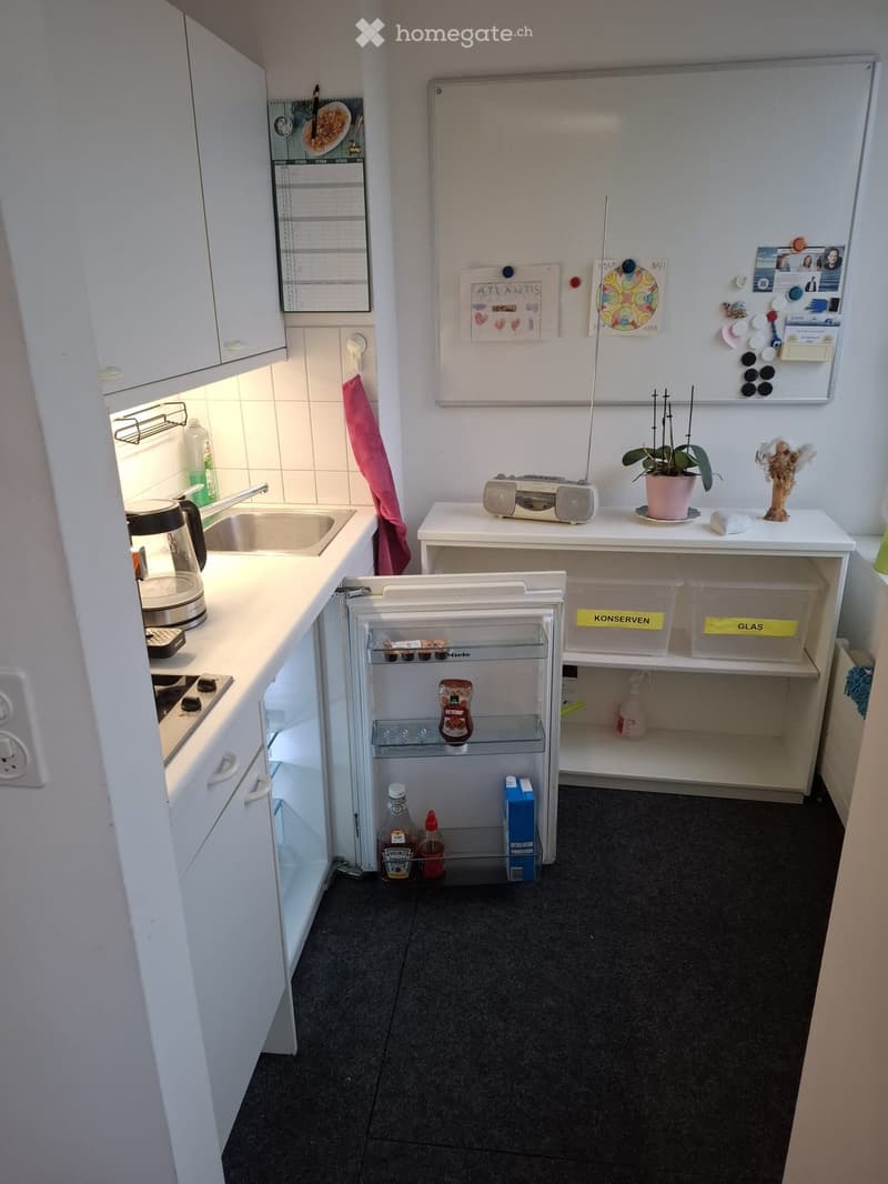 Compact kitchen with white cabinets, a small refrigerator, sink, stove, and a whiteboard with notes and decorations.