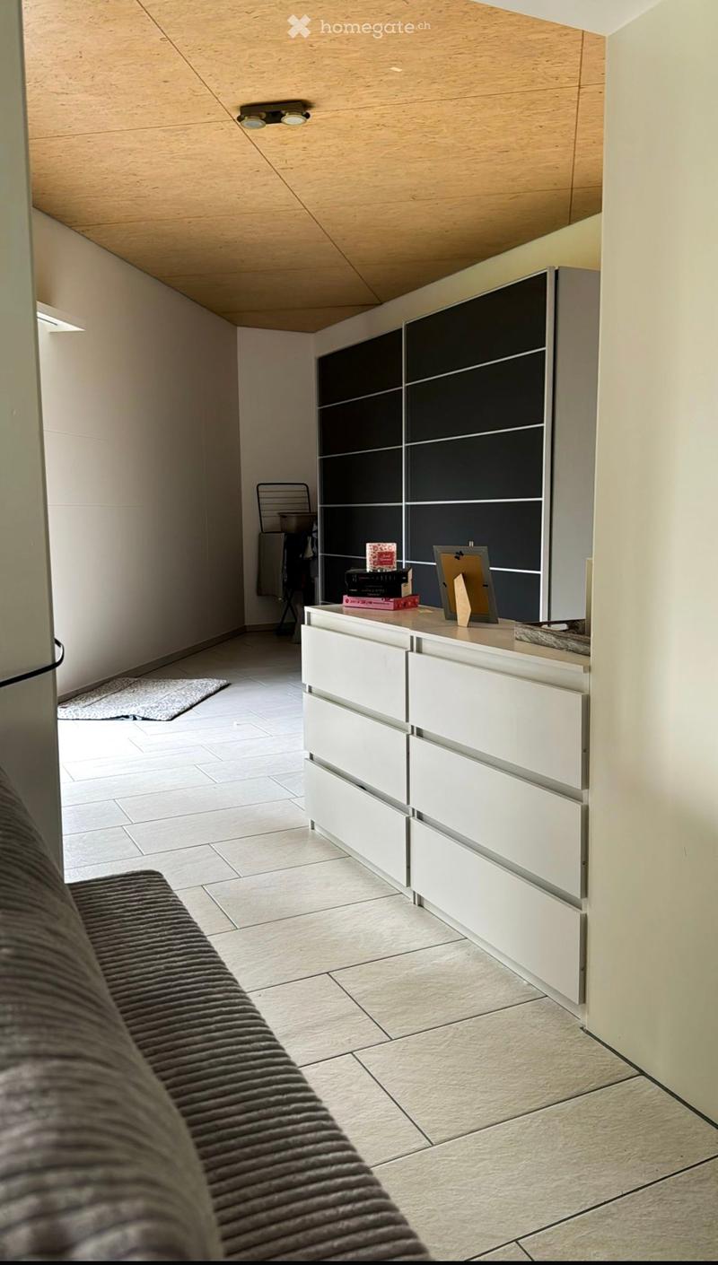 Modern living room with a grey sofa, white cabinet, small table with books and picture frame, and a chair in the background.