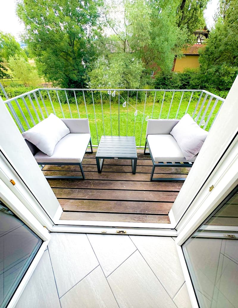 Balcony with wooden decking, metal railing, two grey sofas, and a small table.