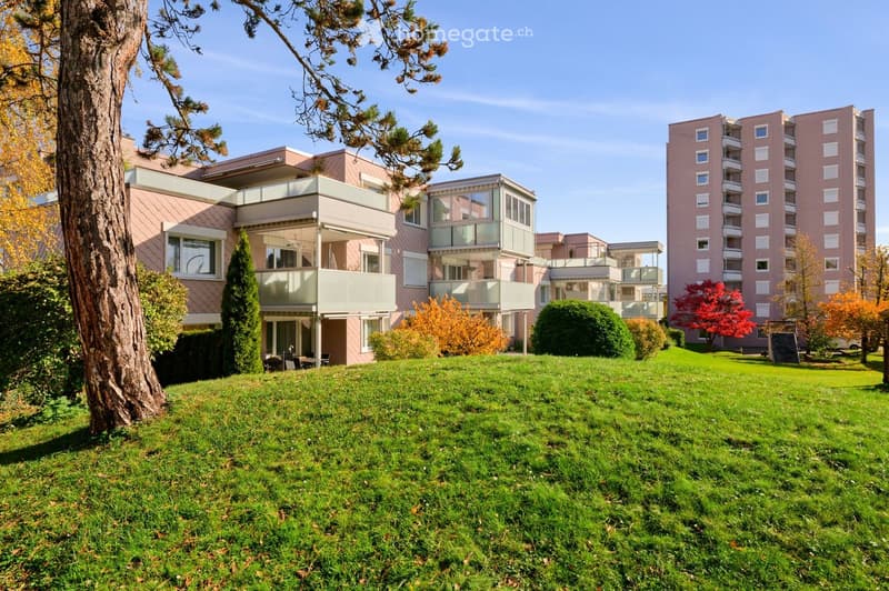 A modern residential complex with a mix of low-rise and high-rise buildings, surrounded by a well-maintained lawn and trees.
