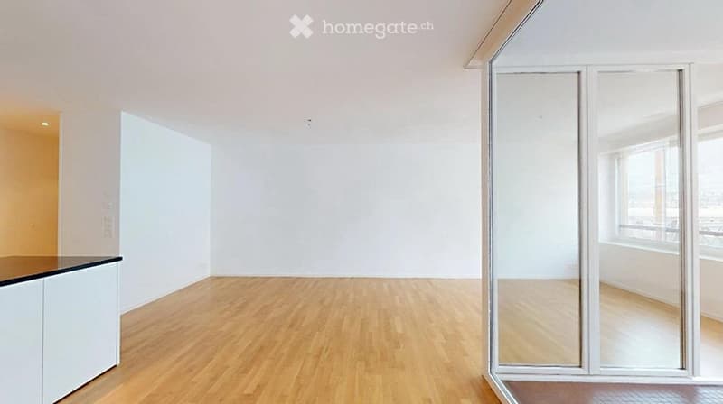 Empty room with light wooden flooring, white walls, and large windows allowing natural light. No furniture or personal items are present.