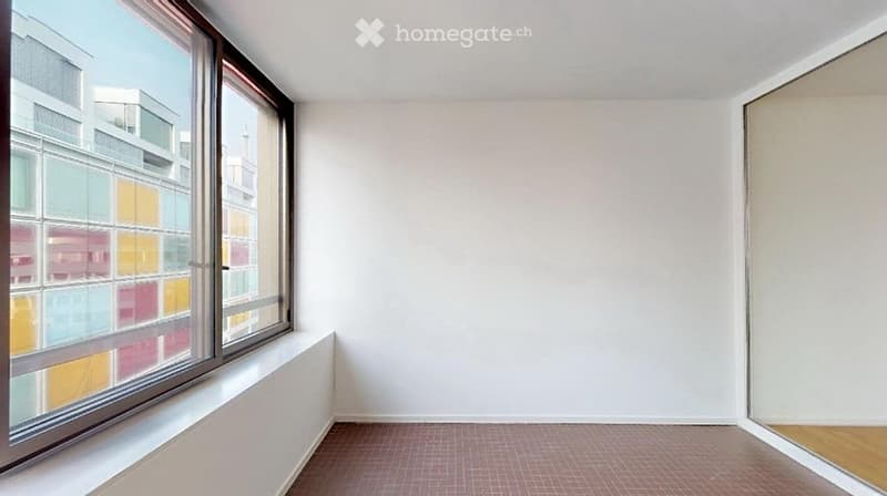 Empty room with white walls, pink tiled floor, large window with colorful glass panels, and a small wooden shelf.