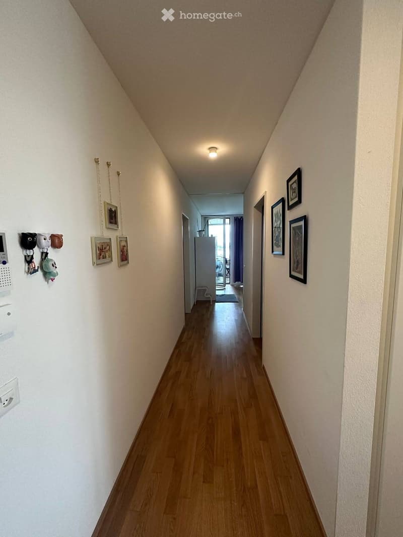 White walls, wooden floor, pictures on wall, lights on ceiling, doors at both ends