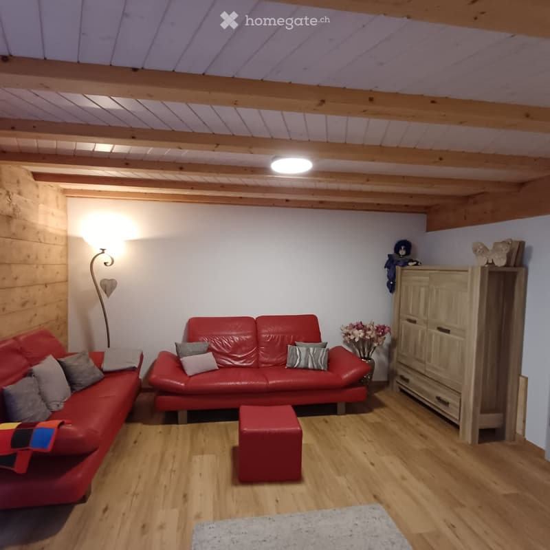 Cozy living room with wooden beams, red leather sofas, a red ottoman, a wooden cabinet, and a floor lamp.