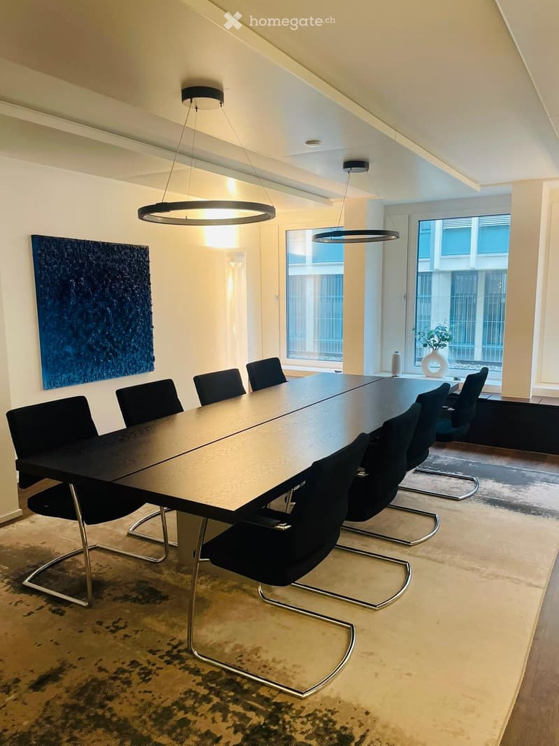 Modern conference room with a long wooden table, black chairs, pendant lights, and a large abstract painting on the wall.