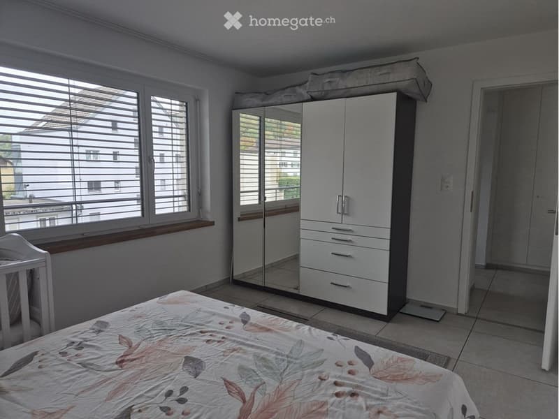 Bright bedroom with a bed, a large mirrored wardrobe, a baby chair, and large windows with blinds.