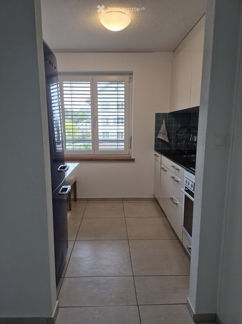 Modern kitchen with white cabinets, tiled floor, and a window with blinds. Features a refrigerator, oven, sink, and faucet.