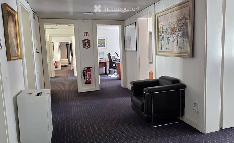 Office hallway with a black leather chair, desk, office chair, and framed artwork on the walls.