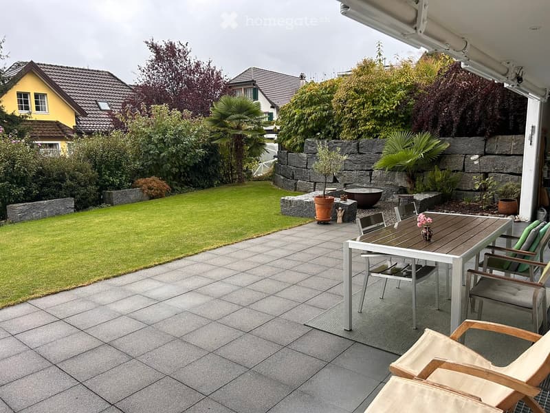 Well-maintained garden with a paved patio, a dining table with chairs, a small potted plant, and a decorative stone wall.