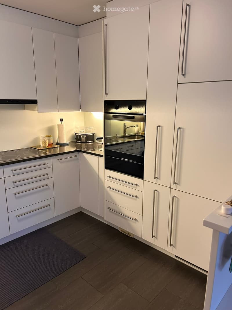 Modern kitchen with white cabinets, stainless steel appliances, and dark wooden flooring.