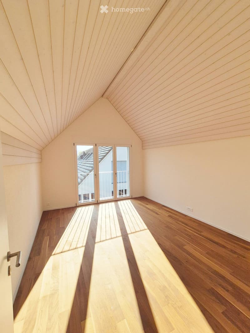 Empty room with wooden flooring, white walls, and large windows with blinds, allowing natural light to fill the space.