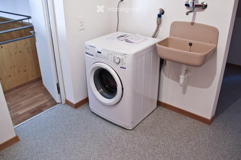 Bathroom with a white washing machine and a beige sink, featuring a tiled wall and wooden trim.