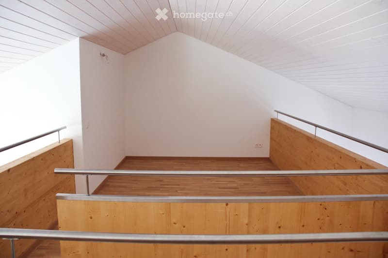 Modern, minimalist staircase with wooden steps and metal railings, white walls, and a slanted ceiling.
