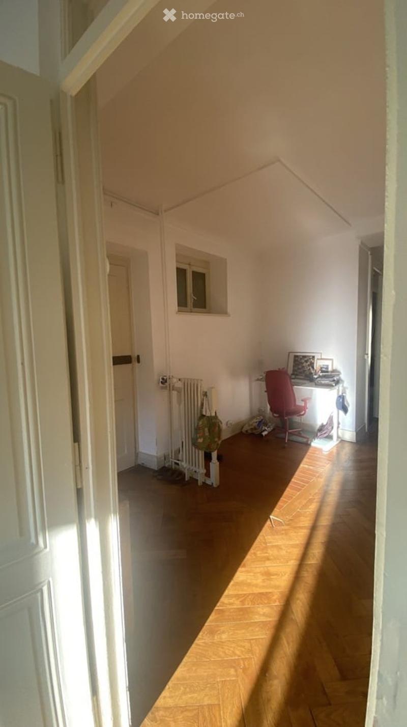 Bright, slanted-ceiling room with wooden flooring, a red chair, a desk, and a radiator near the wall.