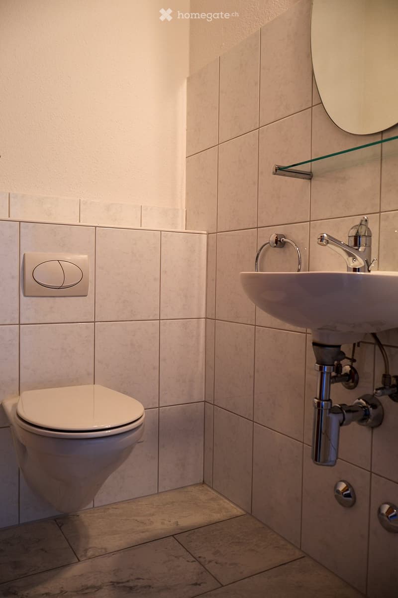 Modern bathroom with a toilet, sink, and mirror. Light-colored tiles and a sleek design.